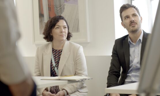 A man and a woman listening intently to a coach whilst looking at a white board